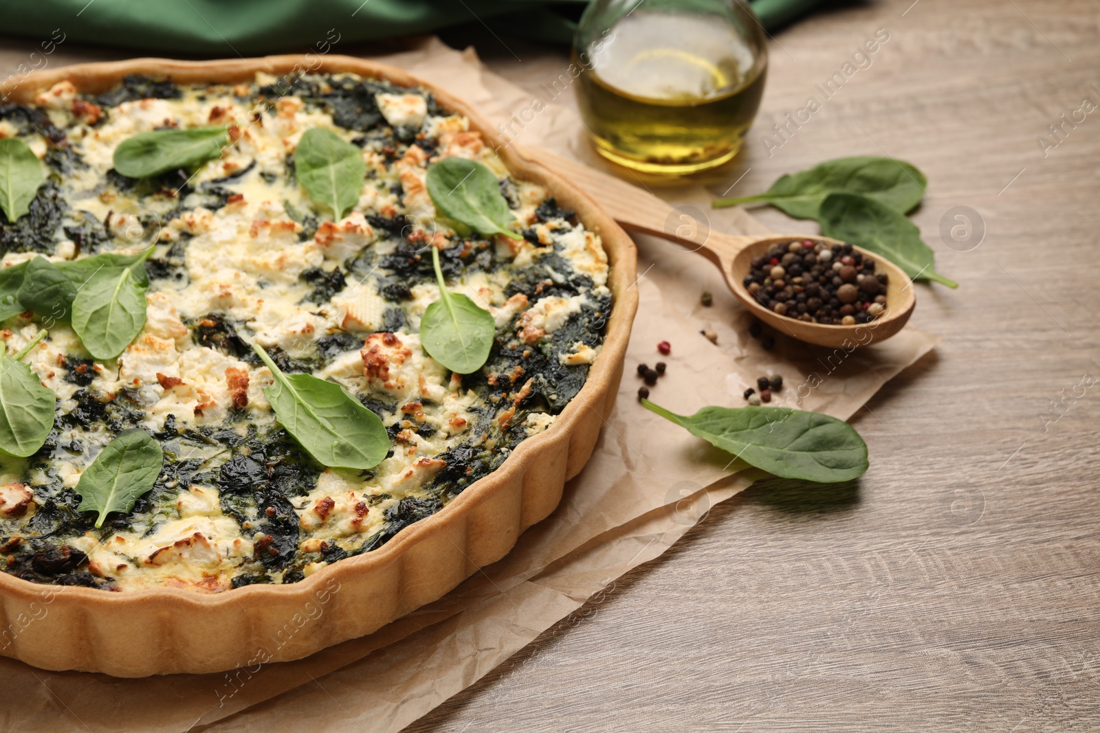 Photo of Delicious homemade quiche, fresh spinach leaves and spices on wooden table