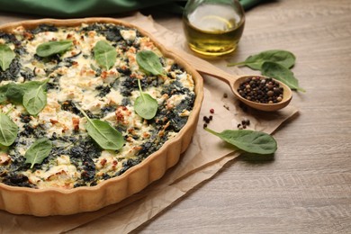 Delicious homemade quiche, fresh spinach leaves and spices on wooden table