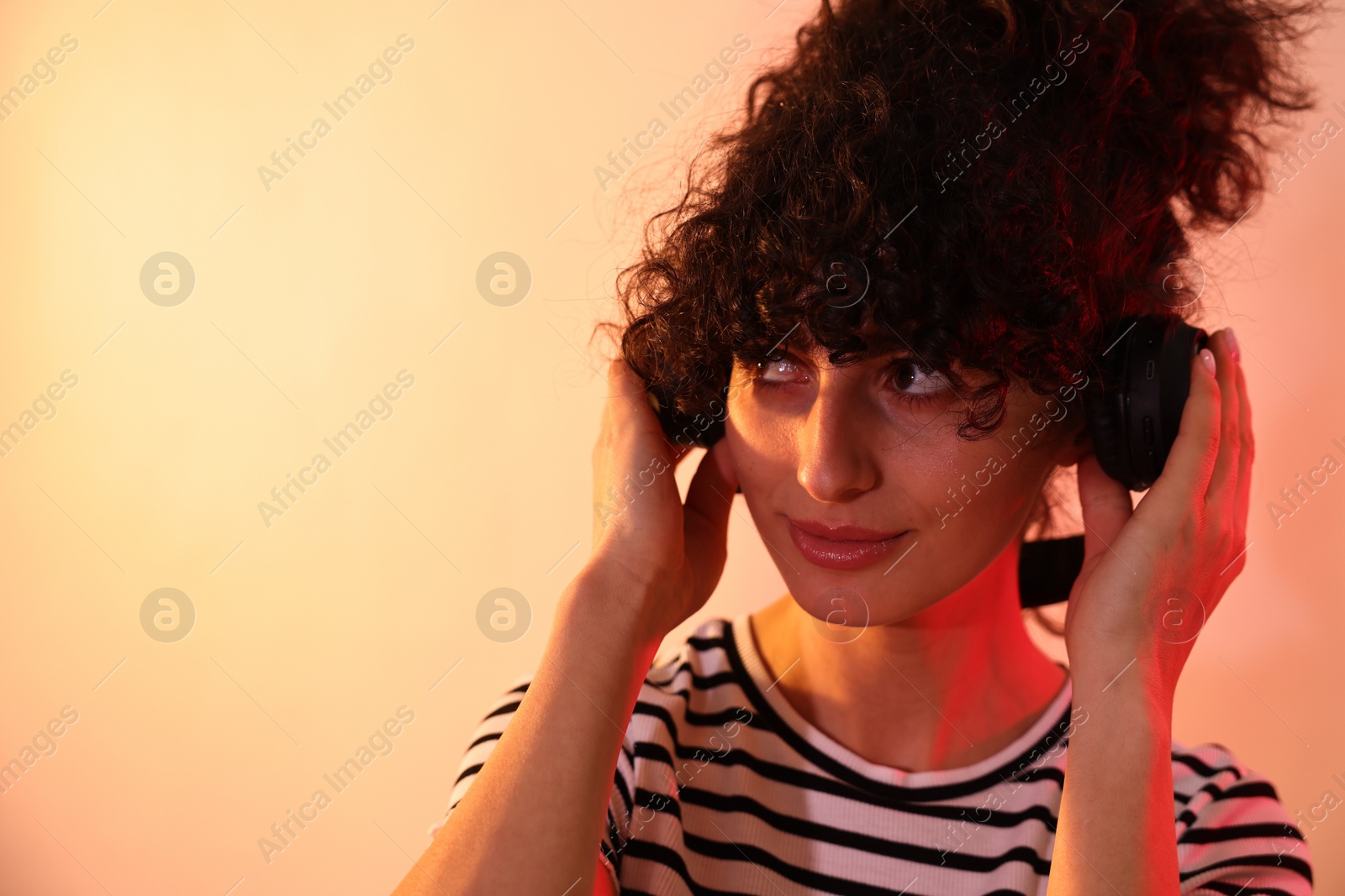 Photo of Beautiful young woman listening to music with headphones on color background in neon lights, closeup. Space for text