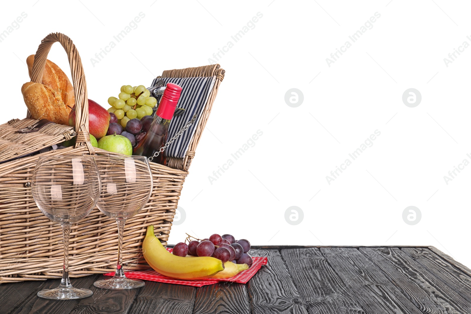 Photo of Wicker picnic basket with wine and different products on wooden table against white background, space for text