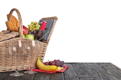 Photo of Wicker picnic basket with wine and different products on wooden table against white background, space for text