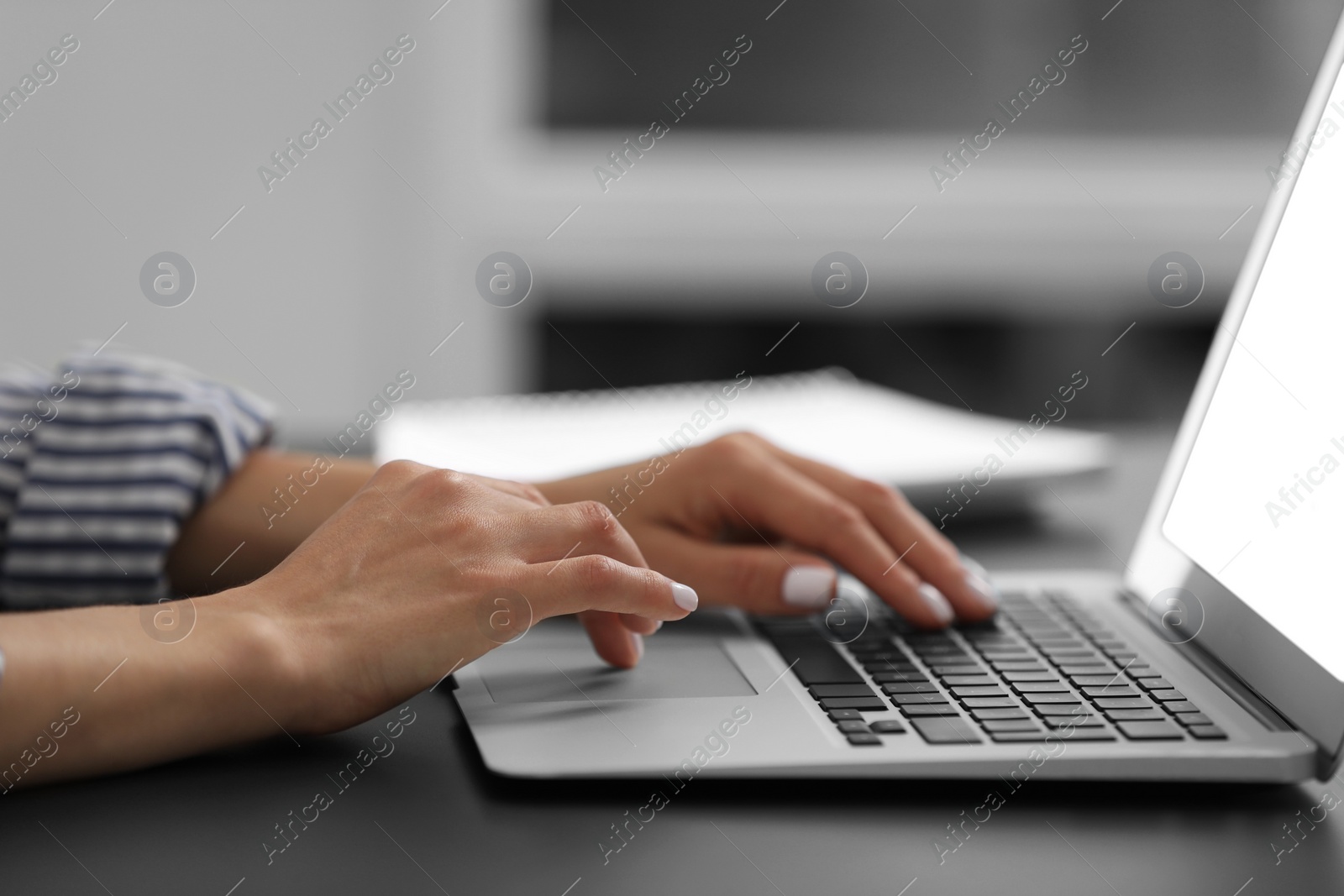 Photo of Woman using modern laptop at black desk in office, closeup