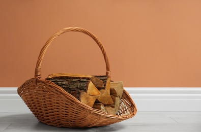 Photo of Wicker basket with firewood near brown wall indoors, space for text