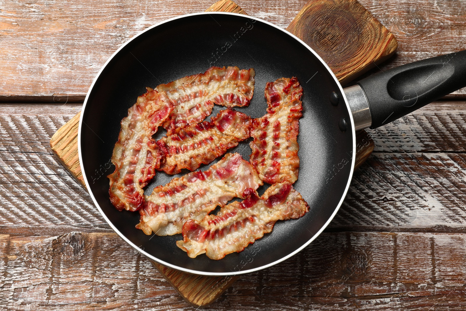 Photo of Delicious bacon slices in frying pan on wooden table, top view