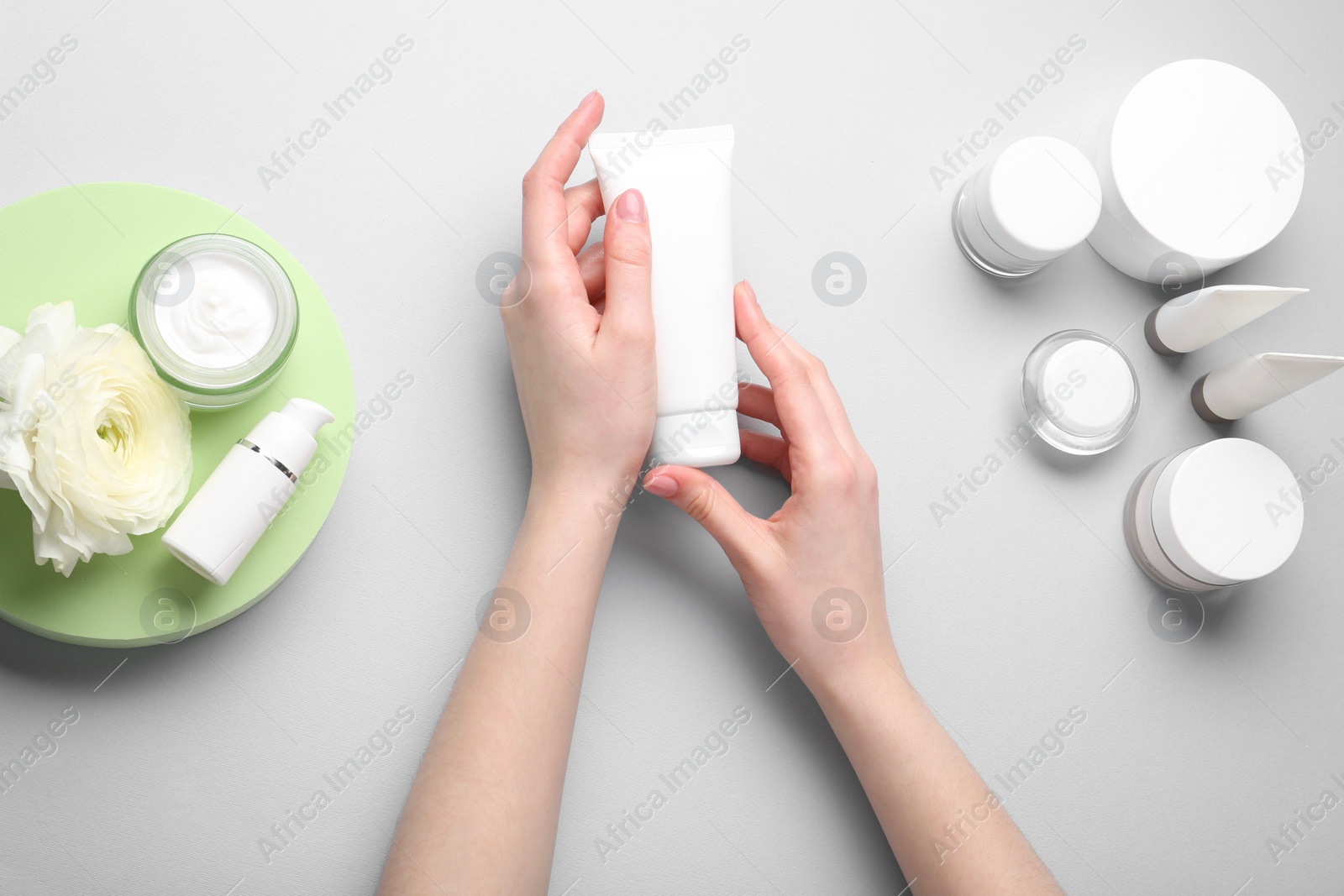 Photo of Woman holding tube of cream on light background, top view