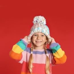 Photo of Cute little girl in hat and warm sweater on red background. Winter season