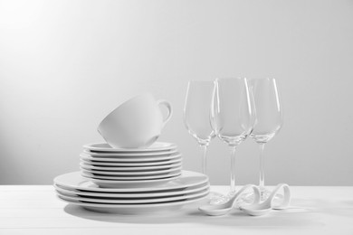 Set of clean dishware and glasses on white wooden table against light background