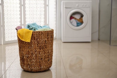 Photo of Wicker laundry basket full of colorful towels on floor in bathroom