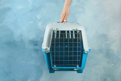 Photo of Woman holding pet carrier against light blue wall, closeup