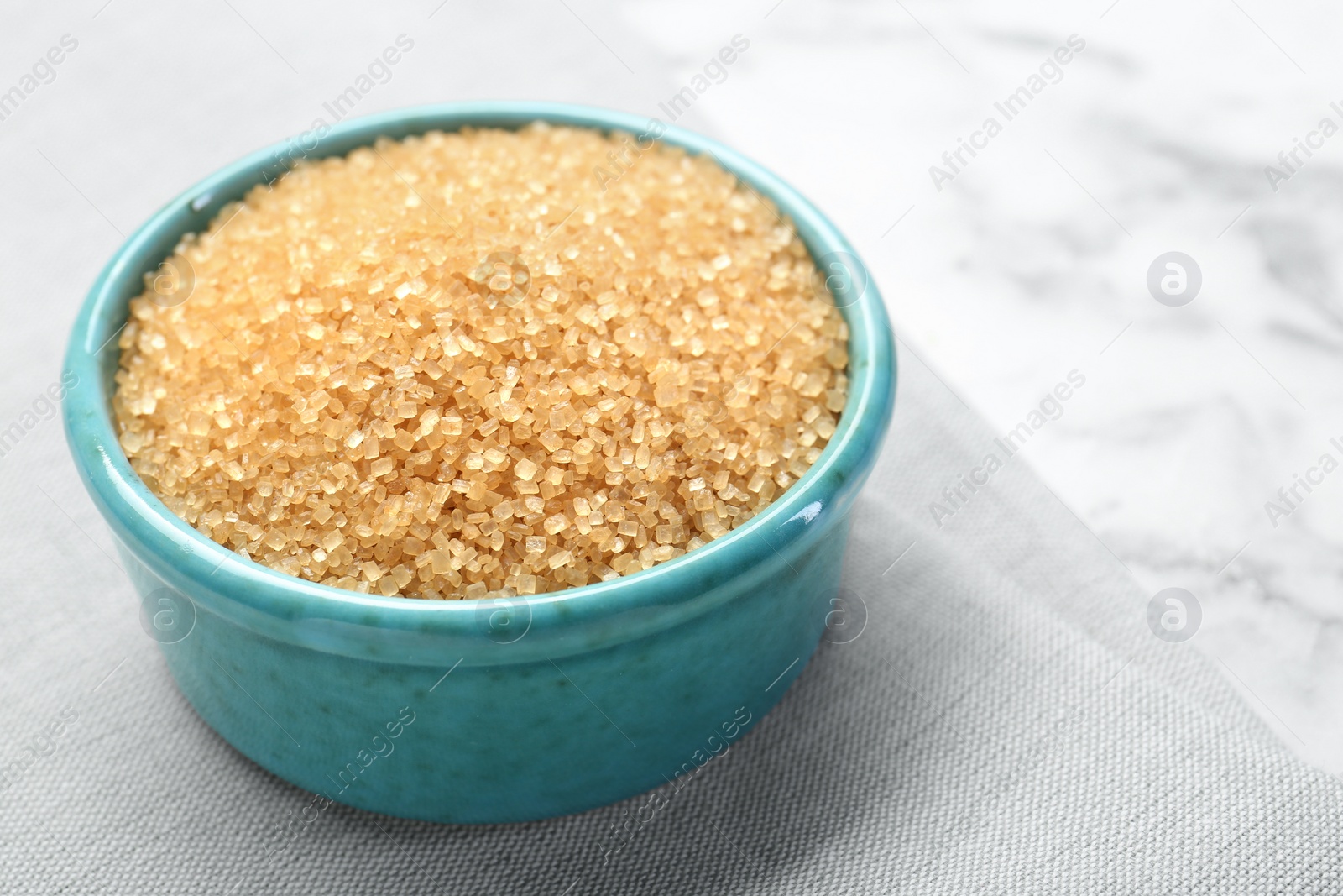 Photo of Brown sugar in bowl on white marble table, closeup. Space for text