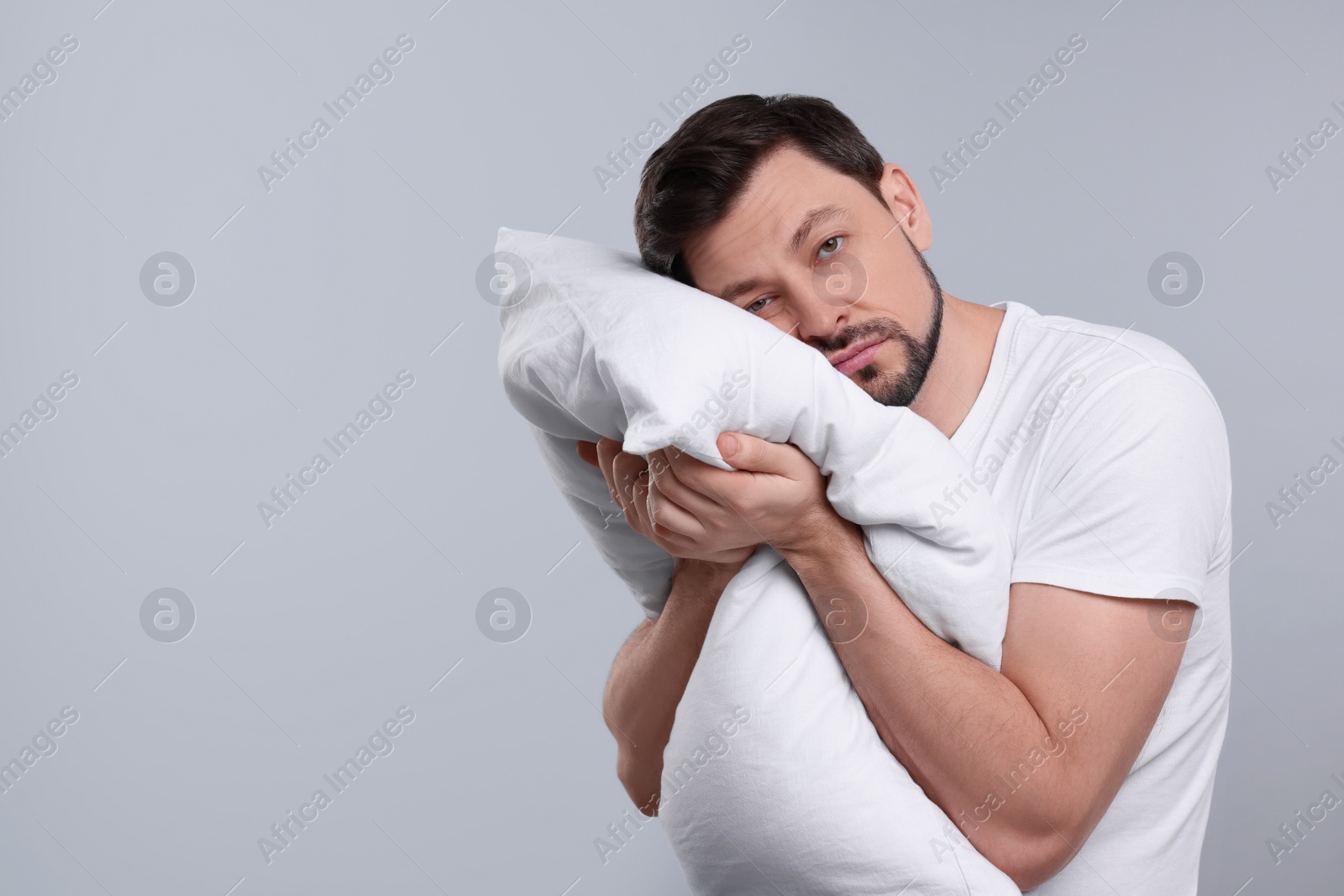 Photo of Tired man with pillow on light grey background, space for text. Insomnia problem