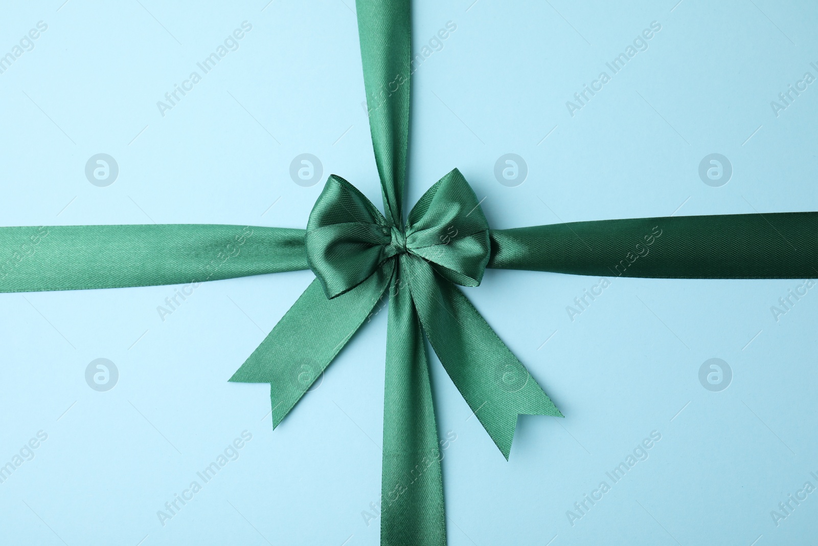 Photo of Green satin ribbon with bow on light blue background, top view