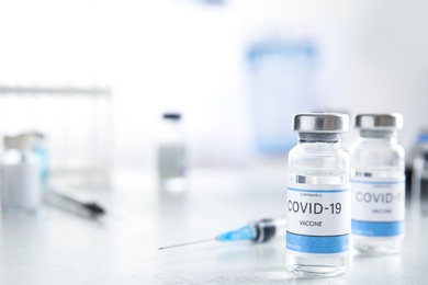 Photo of Vials with vaccine against Covid-19 and syringe on white table indoors. Space for text