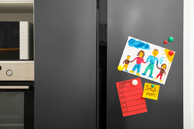 Photo of Modern refrigerator with child's drawing, notes and magnets in kitchen