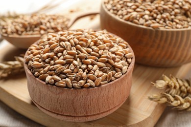 Photo of Wheat grains in bowls on wooden board, closeup
