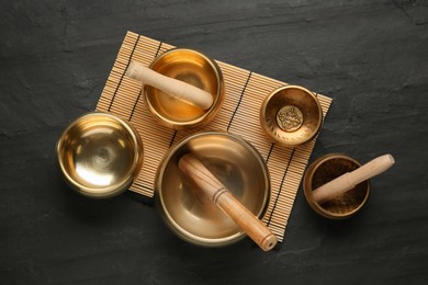 Photo of Golden singing bowls with mallets on black table, flat lay