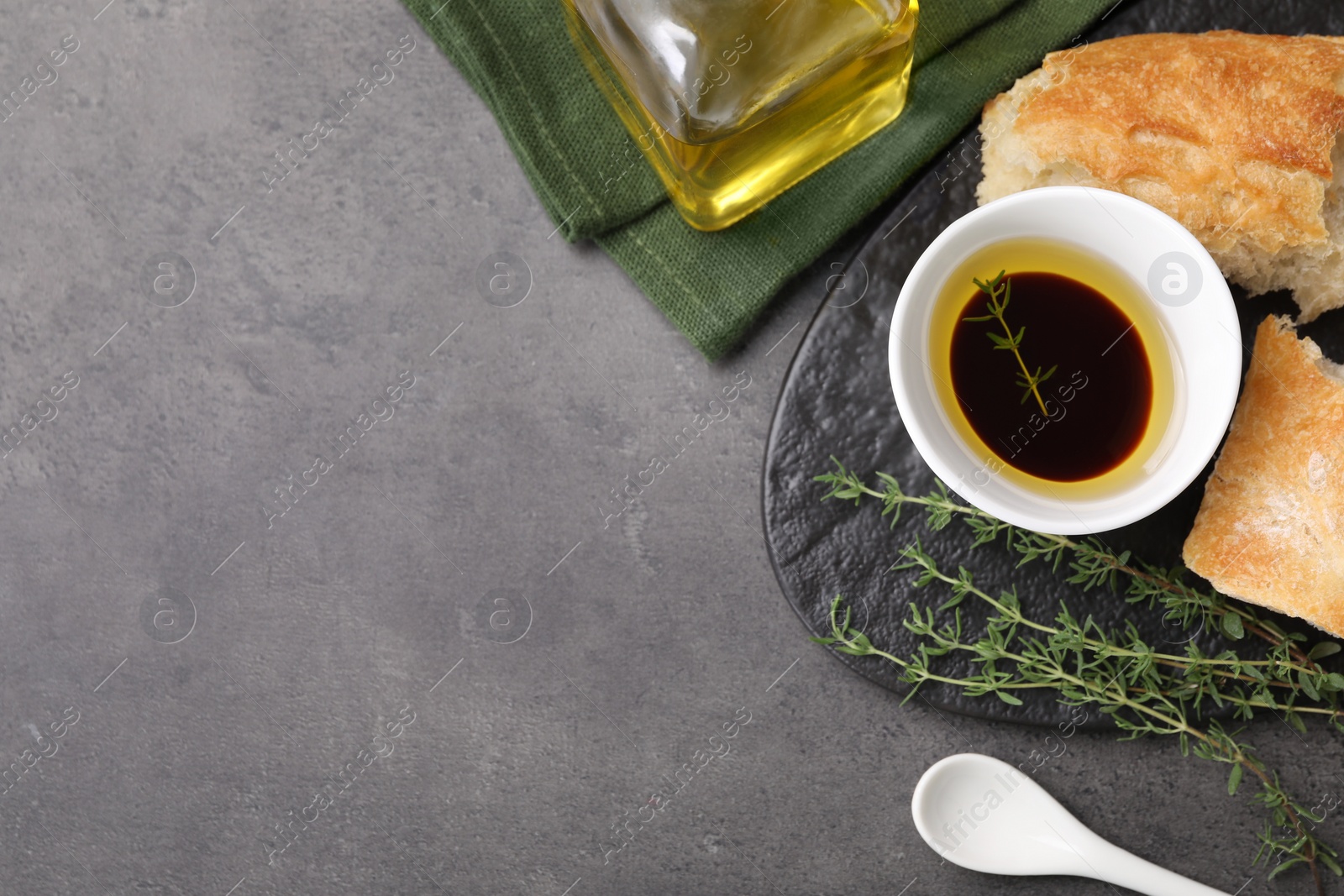 Photo of Bowl of organic balsamic vinegar with oil, thyme and bread on grey table, flat lay. Space for text