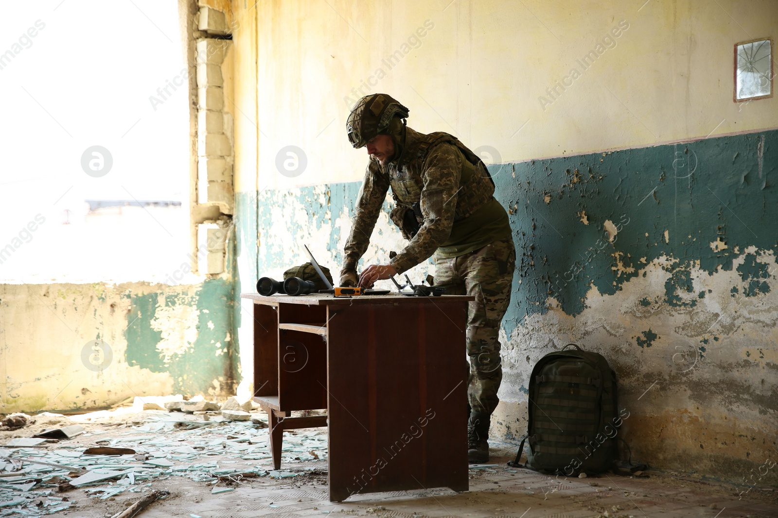 Photo of Military mission. Soldier in uniform using laptop at table inside abandoned building