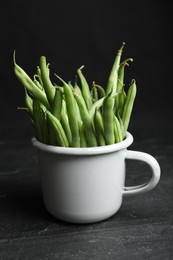 Photo of Fresh green beans in white mug on black table