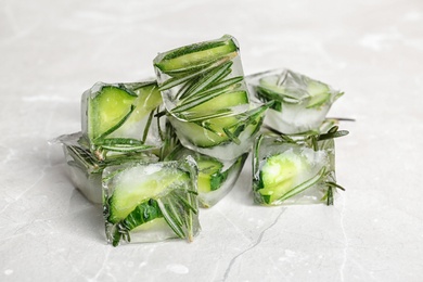 Ice cubes with cut cucumber and rosemary on light background