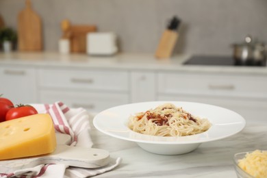 Photo of Delicious pasta with grated cheese and other products on white marble table in kitchen