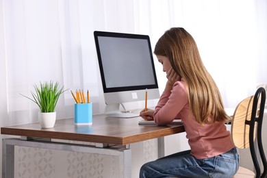 Photo of E-learning. Girl taking notes during online lesson at table indoors
