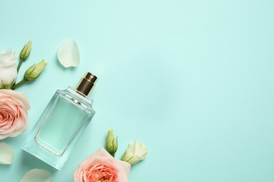 Photo of Flat lay composition with bottle of perfume and flowers on cyan background, space for text