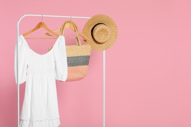 Photo of Rack with accessories and stylish white dress on wooden hangers against pink background, space for text