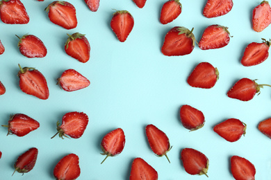 Halves of delicious ripe strawberries on light blue background, flat lay