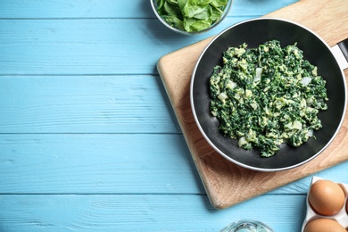 Photo of Flat lay composition of tasty cooked spinach and space for text on light blue wooden table. Healthy food