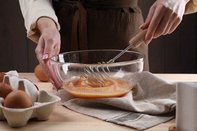 Photo of Woman whisking eggs in bowl at table, closeup