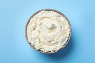 Photo of Bowl of tasty cream cheese on light blue background, top view