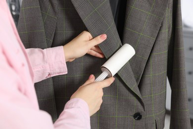 Photo of Woman cleaning suit with lint roller, closeup