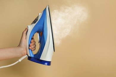 Woman holding modern iron with steam on beige background, closeup. Space for text