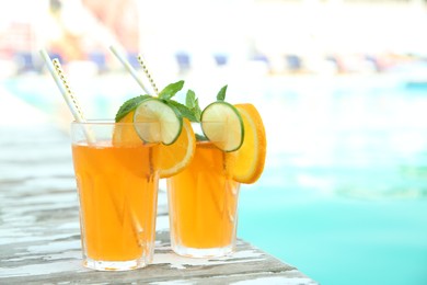 Photo of Refreshing cocktail in glasses near outdoor swimming pool on sunny day