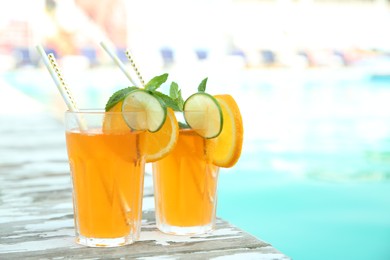 Refreshing cocktail in glasses near outdoor swimming pool on sunny day