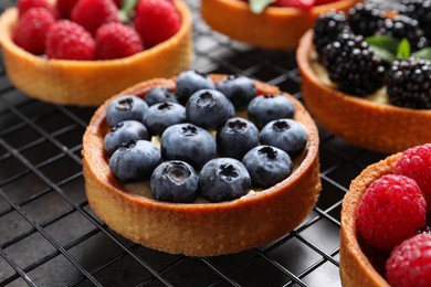 Tartlets with different fresh berries on cooling rack, closeup. Delicious dessert