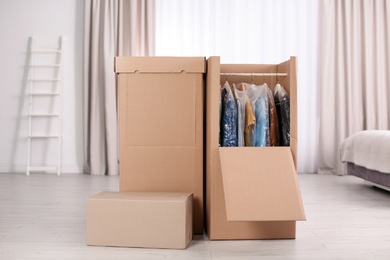 Photo of Cardboard wardrobe boxes with clothes on hangers in bedroom