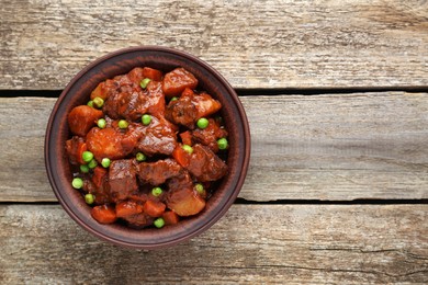 Delicious beef stew with carrots, peas and potatoes on wooden table, top view. Space for text