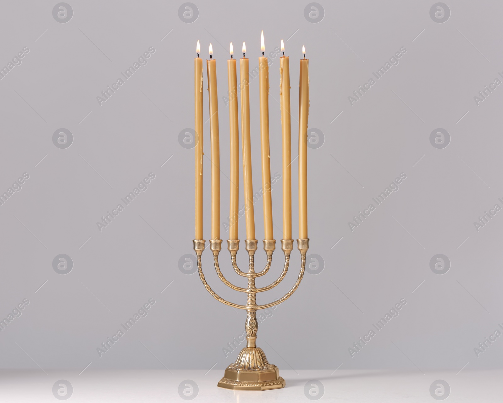 Photo of Golden menorah with burning candles on table against light grey background