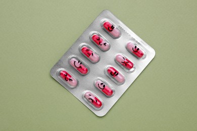 Antidepressants with different emoticons on light green background, top view