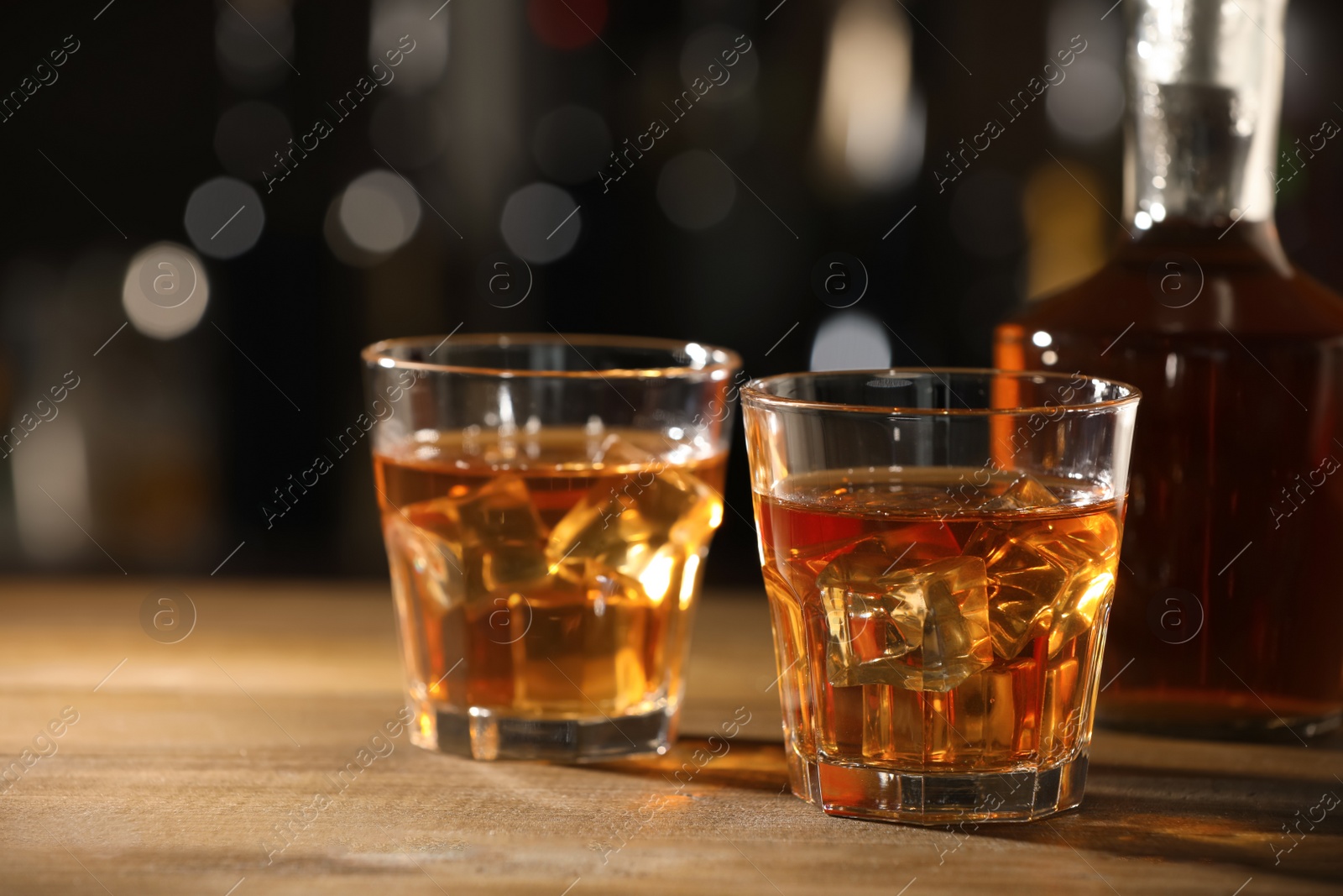 Photo of Glasses of whiskey with ice on wooden table in bar, space for text