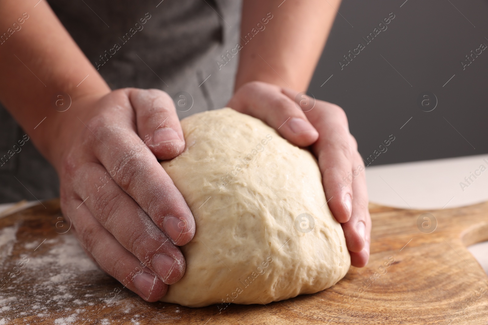 Photo of Man kneading dough at table near grey wall, closeup