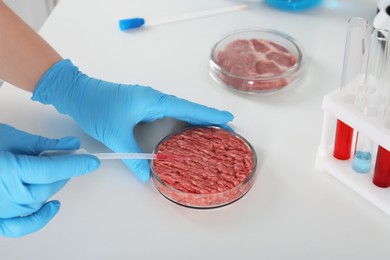 Photo of Scientist dripping sample onto raw minced cultured meat at table in laboratory, closeup