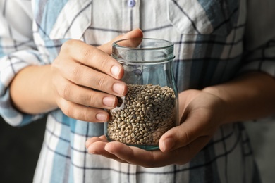 Photo of Woman holding jar of organic hemp seeds, closeup