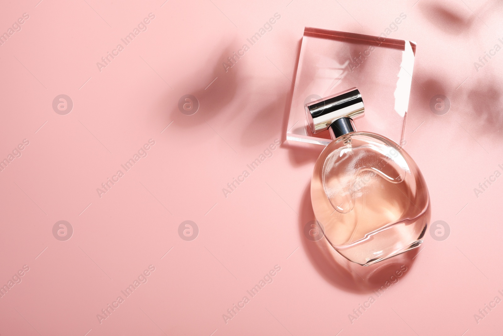 Photo of Bottle of luxury women's perfume in sunlight on pink background, top view. Space for text