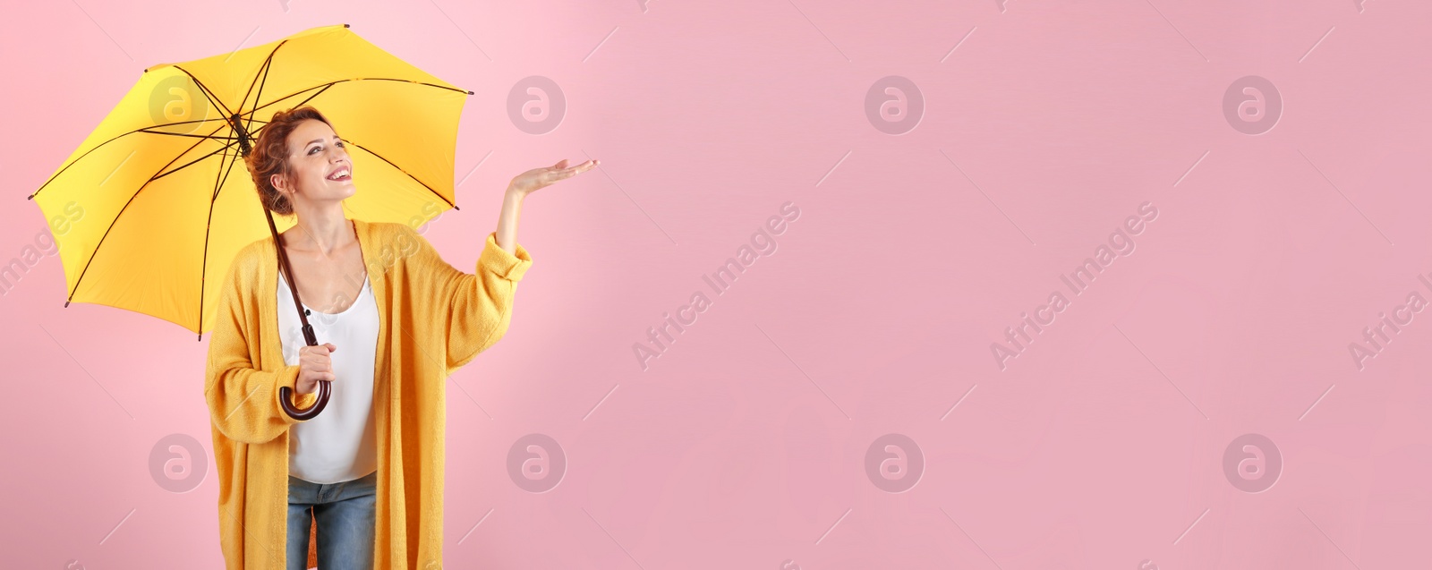 Image of Autumn season. Happy woman with yellow umbrella on pink background, space for text. Banner design
