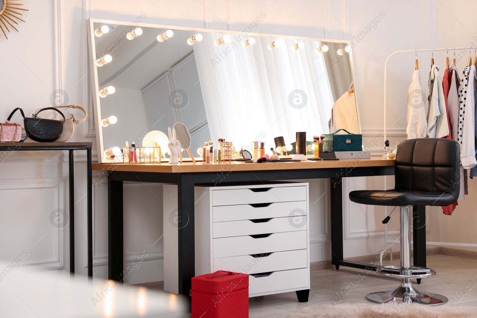 Photo of Makeup room. Stylish dressing table with mirror, chair and clothes rack