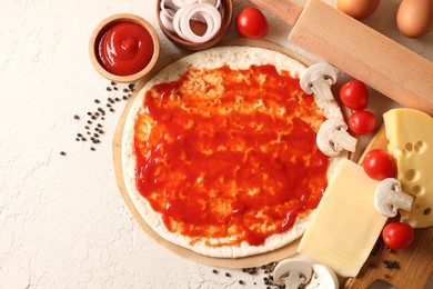 Photo of Pizza base smeared with tomato sauce, peppercorns and products on light textured table, flat lay