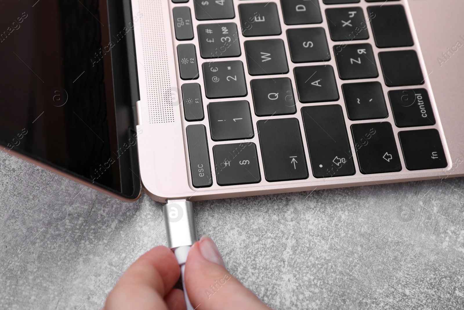 Photo of Woman plugging USB cable into laptop port at grey table, closeup